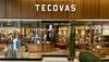 The image shows the word "Tecovas" written in a cursive font on a patchwork background of various shades of brown leather.