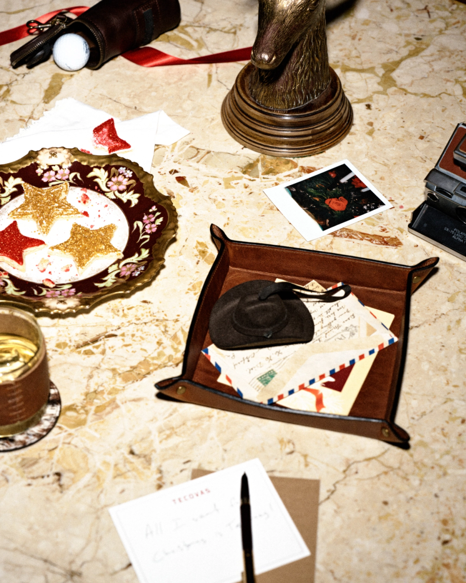 A marble tabletop with a decorative plate of glittery star cookies, a miniature cowboy hat on top of letters in a leather tray, a polaroid photo, and a handwritten note with a pen.