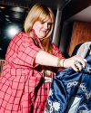 Person in a red plaid shirt examines a piece of blue patterned clothing, with a focused expression.