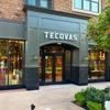 The image shows the word "Tecovas" written in a cursive font on a patchwork background of various shades of brown leather.