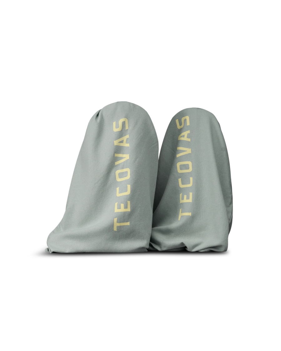 The Annie in Slate Blue Cowhide. Two light gray boot bags with "Tecovas" printed in large yellow letters on each, placed side by side against a plain white background.