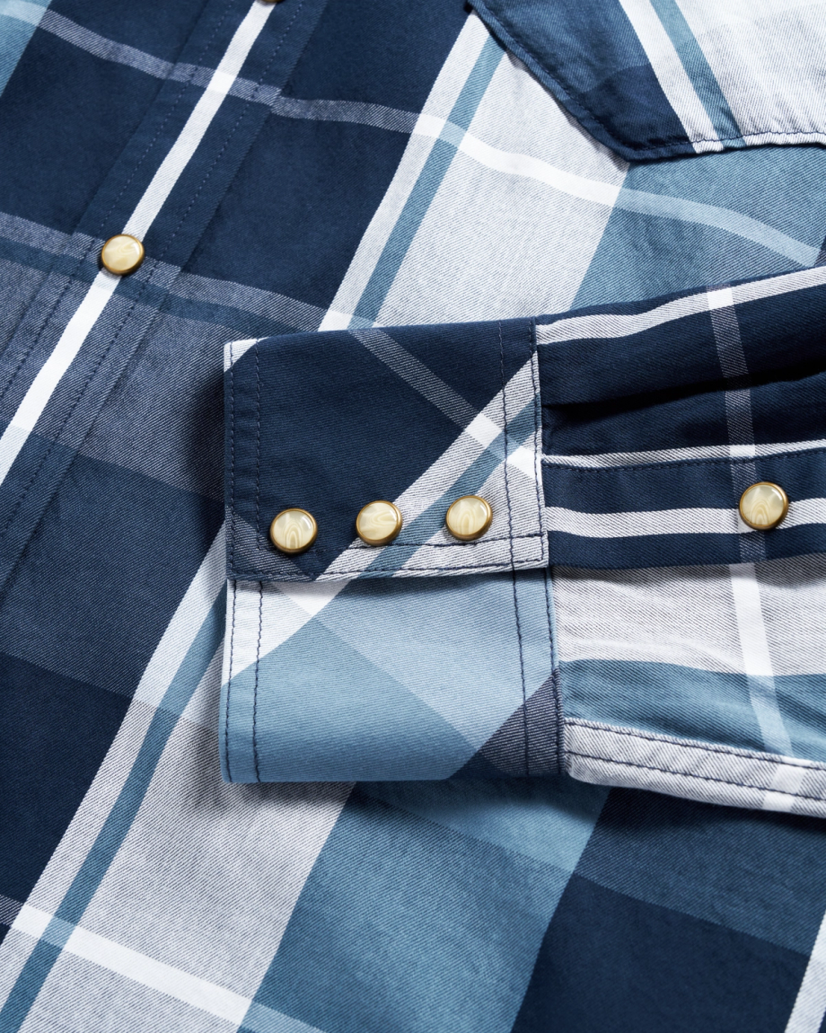 Close-up of a blue and white plaid shirt sleeve with three gold buttons on the cuff.