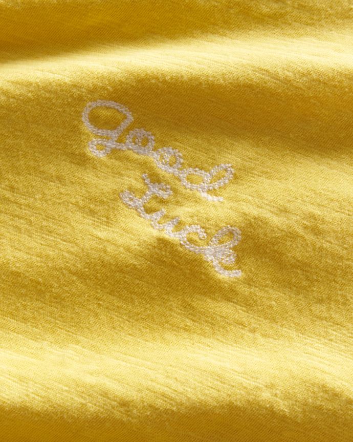 Up-close view of the stitching on the Women's Vintage Ringer Tee in the color Golden Yellow/Tan that reads "good luck" in cursive.