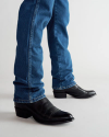 A person wearing straight-cut blue jeans and black leather cowboy boots standing on a white background.