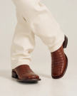 Close up of a person wearing cream pants and The William Caiman cowboy boots in rich Dark Pecan Caiman leather.