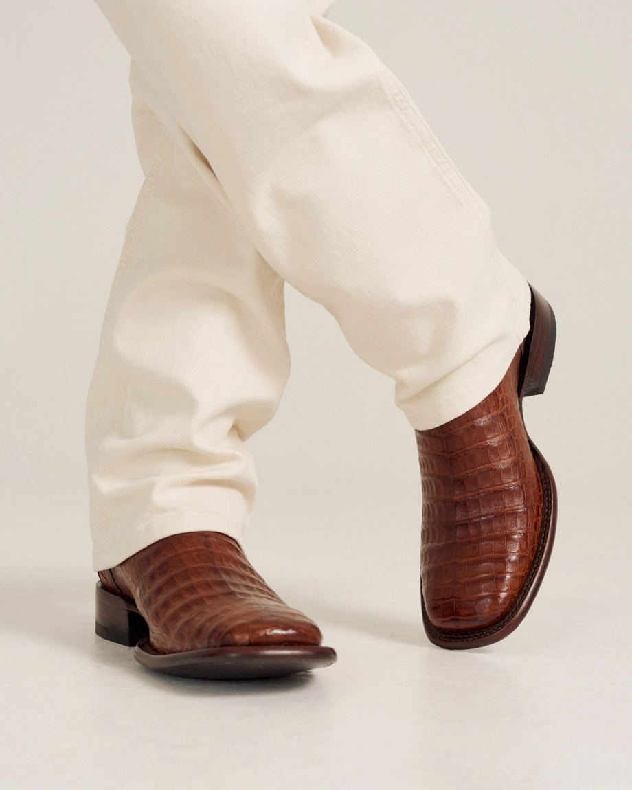 Close up of a person wearing cream pants and The William Caiman cowboy boots in rich Dark Pecan Caiman leather.