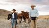 Cowgirl and cowboy leading horses through the desert