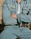 A person wearing a light denim jacket and jeans with a white undershirt, arms crossed, and face not visible in the image.