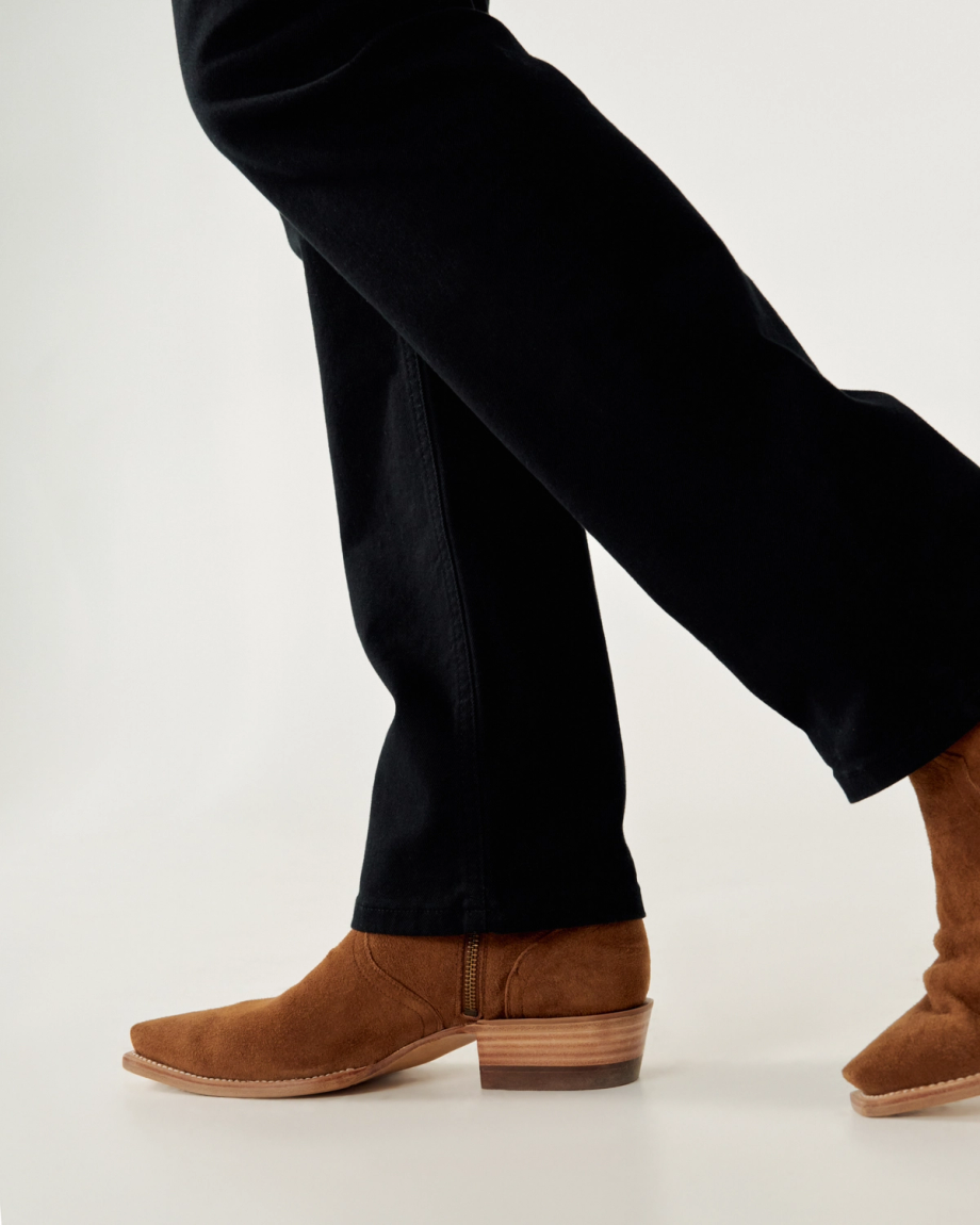Person wearing dark pants and brown suede cowboy boots, walking on a light background.
