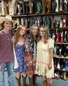 Four people wearing casual outfits and cowboy boots stand in front of shelves filled with various cowboy boots in a store.