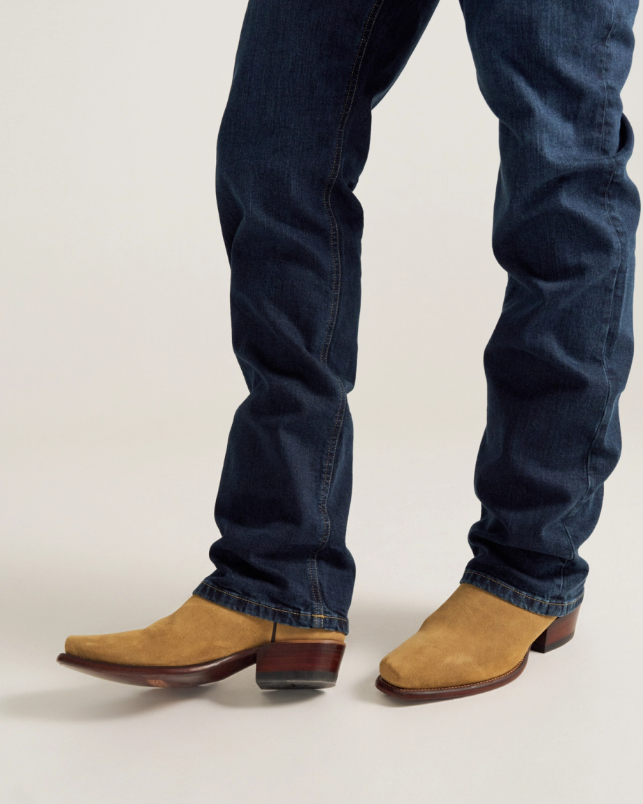 Person wearing blue jeans and tan suede cowboy boots, standing on a light-colored surface.