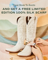 A pair of white cowboy boots displayed upright, with hands tying a silk scarf around them, against a pastel striped background. text overhead promotes a limited edition gift.