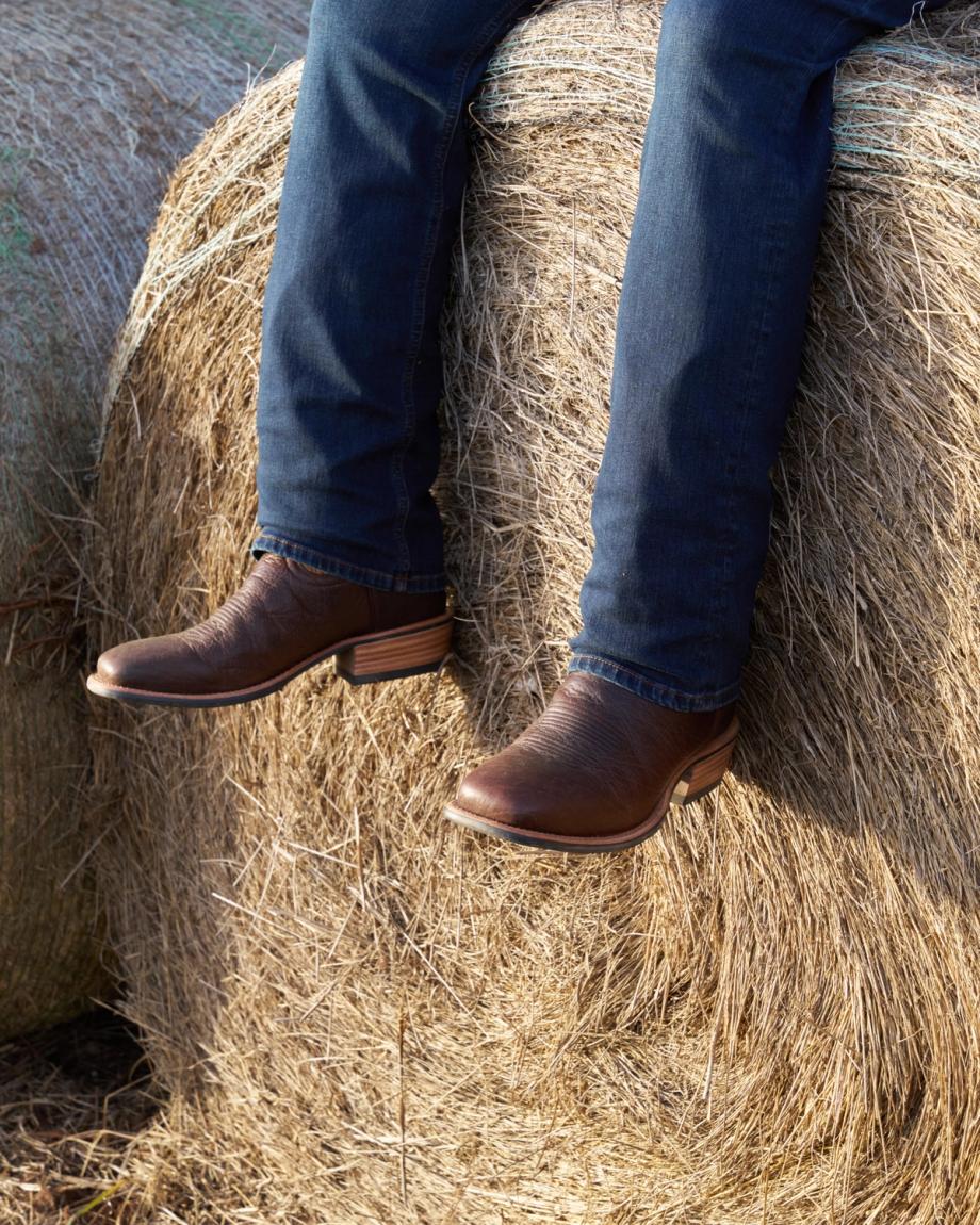 Man wearing the cody chocolate sitting on a barrel of hay