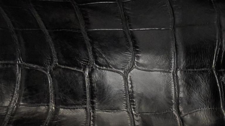 Close-up of shiny black leather with an embossed crocodile skin pattern.