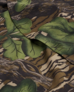 A close-up of fabric featuring a camouflage pattern with green leaves and brown, beige, and black shapes resembling tree bark.
