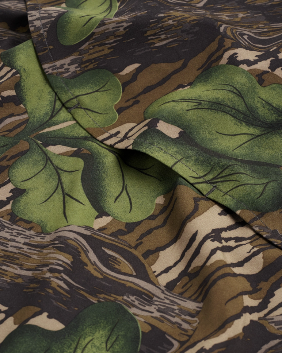 A close-up of fabric featuring a camouflage pattern with green leaves and brown, beige, and black shapes resembling tree bark.