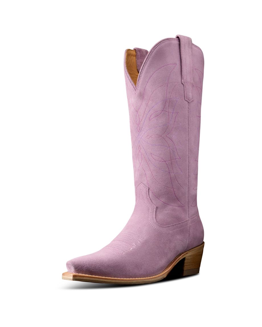 The Annie in Lavender Suede. A single pink Annie Suede cowboy boot with decorative stitching, a pointed toe, wooden heel, and pull tabs on either side.