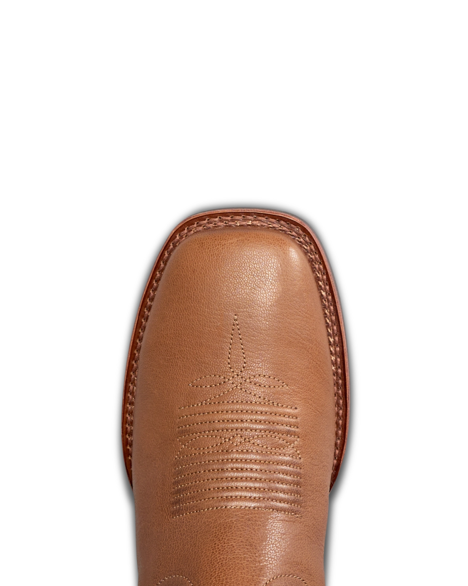 The Dusty in Mesa Goat. Close-up view of the toe of a tan leather cowboy boot from The Dusty Goat, featuring decorative stitching and a square toe design, shown on a white background.
