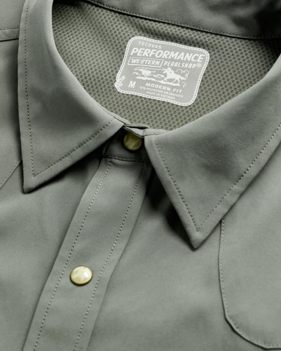 Close-up of a grey T-shirt featuring pearl snap buttons and a label reading "Tecovas Performance Western Pearl Snap, Medium, Modern Fit.