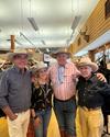 Four people wearing cowboy hats and casual attire are standing together in a western-themed store. Mounted deer heads and shelves with various items are visible in the background.