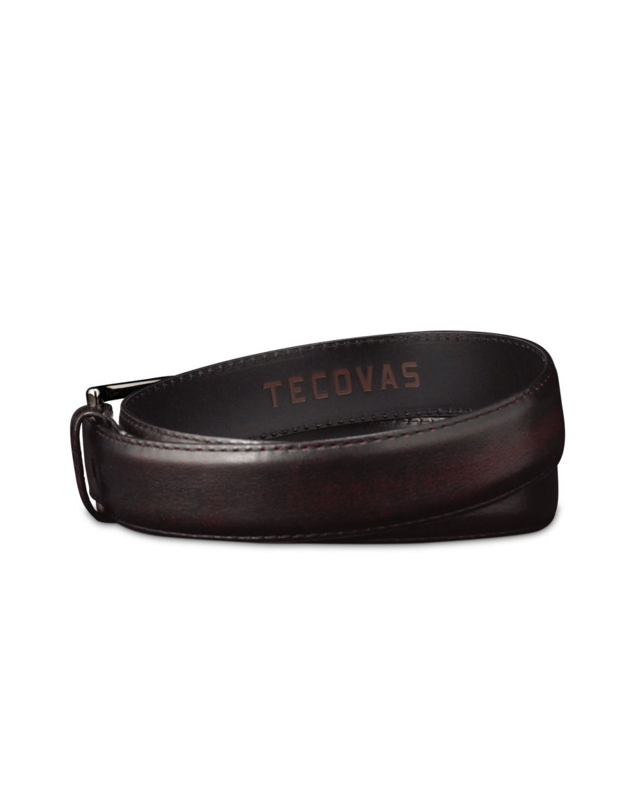 A dark brown leather belt with a silver buckle, embossed with the brand name "Tecovas" on the inner side, coiled in a loop against a black background.