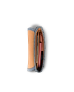 Top view of an open, slim pouch containing a brown notebook, a pink pen, and other small items, all organized neatly inside.