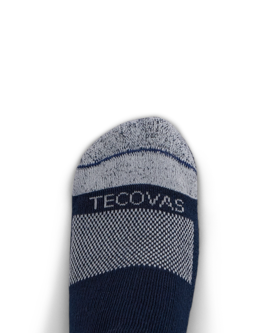 A close-up of a foot wearing a navy and gray sock with the word “Tecovas” woven across the top.
