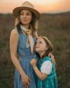 Kelly Colchin wearing a cowboy hat and her daughter smiling while looking at her in the field.