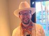A man wearing a hat and glasses is smiling.