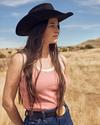Woman on a ranch wearing a pink tank top and cowgirl hat