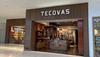 Storefront of Tecovas in a shopping mall, featuring leather goods and boots displayed inside, with glass walls and large illuminated signage above the entrance.
