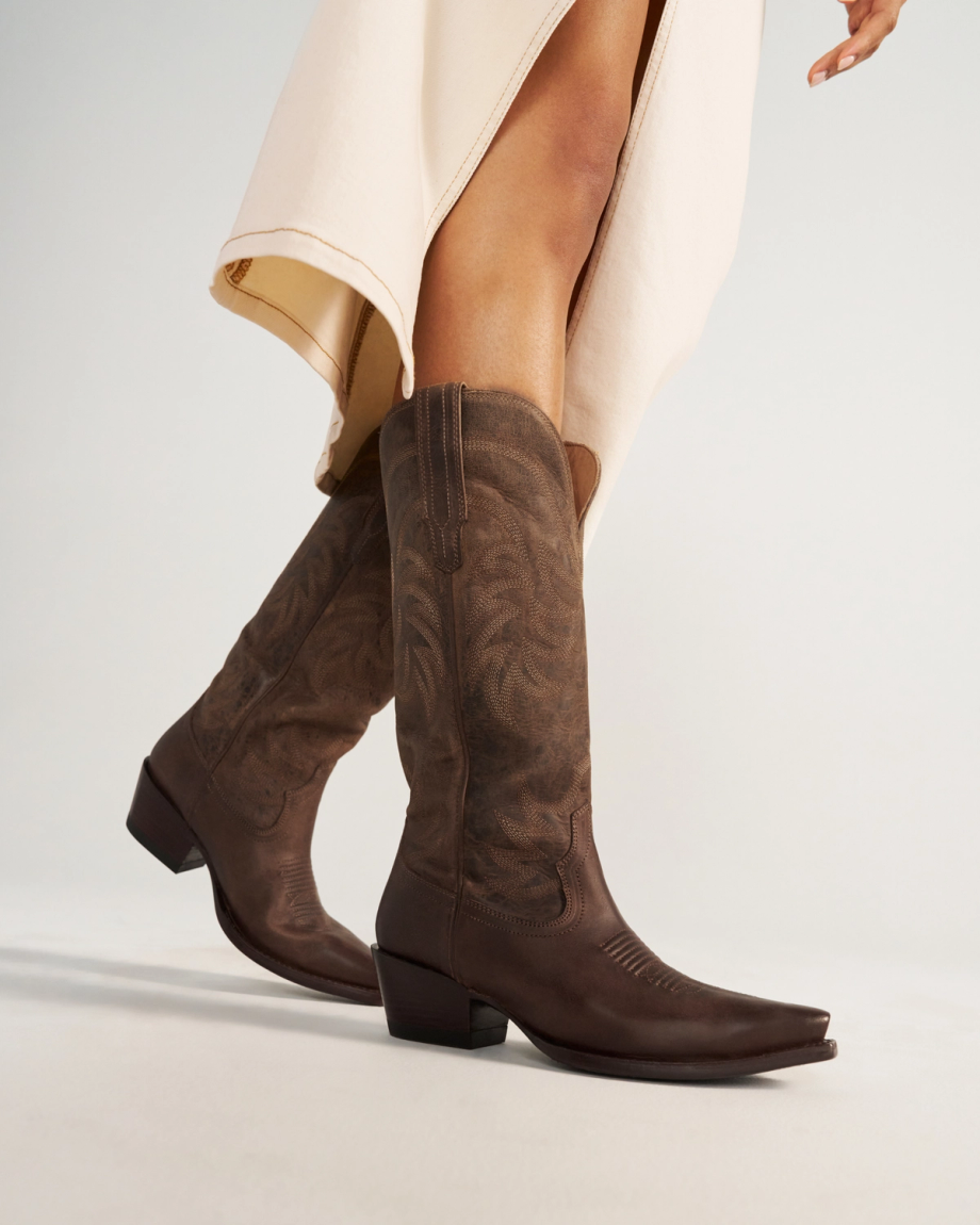 The Annie in Cafe Goat. A person wearing a cream-colored skirt and dark brown cowboy boots stands on a light surface, capturing the cozy charm of Cafe Goat.