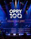 Stage with "OPRY 100 GRAND OLE OPRY" illuminated on a large screen, musical instruments set up, and colorful lights shining down.