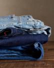 A neatly folded stack of three pairs of jeans in different denim shades placed on a wooden surface.