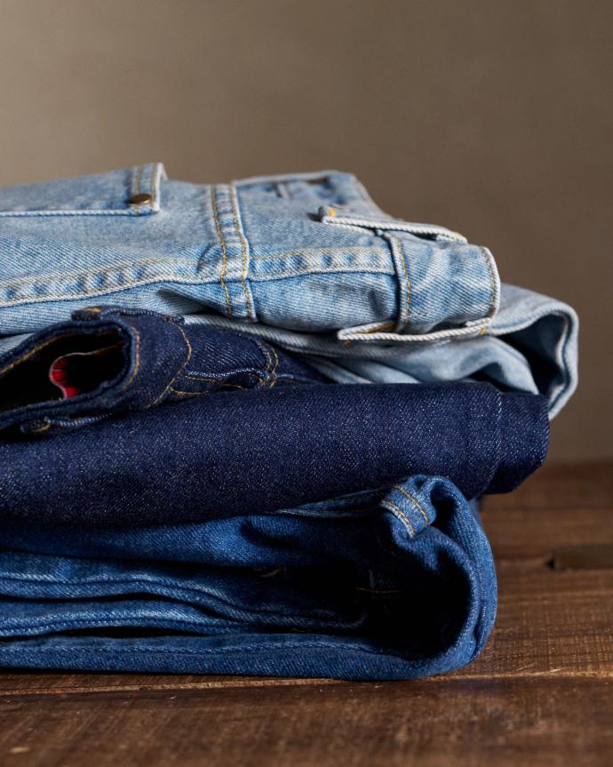 A neatly folded stack of three pairs of jeans in different denim shades placed on a wooden surface.