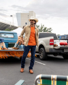 Man at a tailgate wearing an orange t shirt and cowboy hat standing in a parking lot outside of a stadium