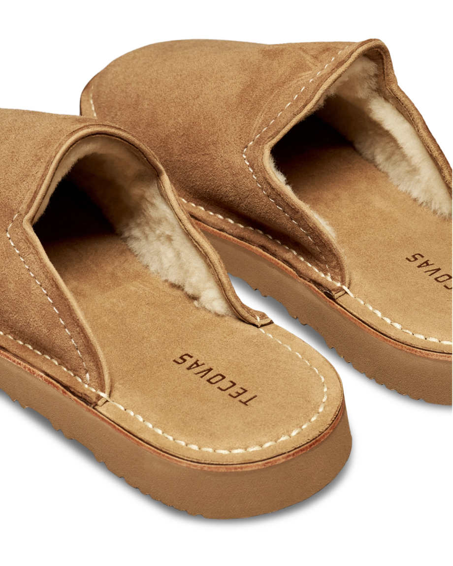 The Oliver in Cognac Suede with Shearling. Pair of cognac suede slip-on slippers with shearling lining and Tecovas branding on the footbed.