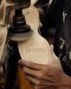 A person uses a polishing tool on the leather sole of a shoe labeled "TECOVAS," holding it steady with one hand.