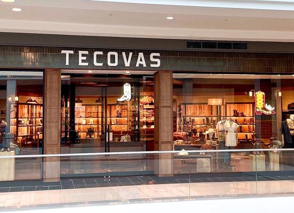 Storefront of Tecovas in a shopping mall, displaying boots, hats, and Western-style clothing inside with warm lighting.