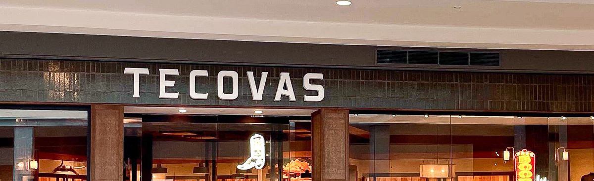 Storefront of Tecovas in a shopping mall, displaying boots, hats, and Western-style clothing inside with warm lighting.