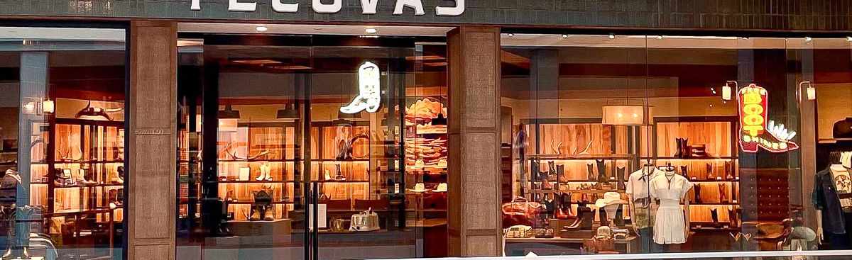 Storefront of Tecovas in a shopping mall, displaying boots, hats, and Western-style clothing inside with warm lighting.