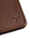 Close-up of a brown leather wallet corner featuring a small embossed logo resembling the letter "T.