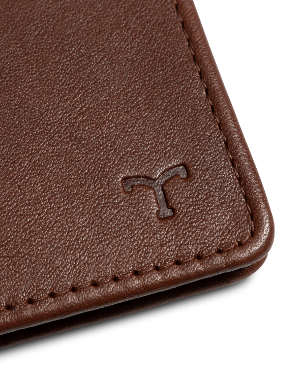 Close-up of a brown leather wallet corner featuring a small embossed logo resembling the letter "T.