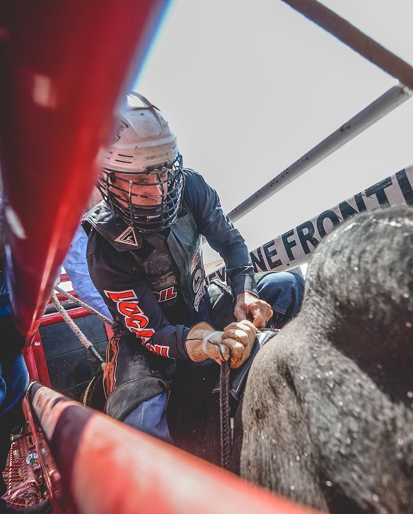 A bull rider in protective gear grips a rope while preparing to ride inside a rodeo chute.