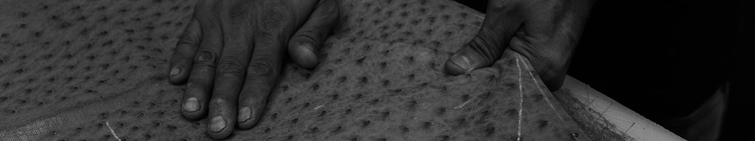 Two hands are working with a piece of textured material, possibly animal leather, on a flat surface.