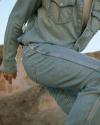 A person wearing a denim jacket and jeans is captured mid-step outdoors with rocky terrain in the background.