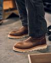 Person wearing brown leather boots and black jeans, seated on a concrete floor.