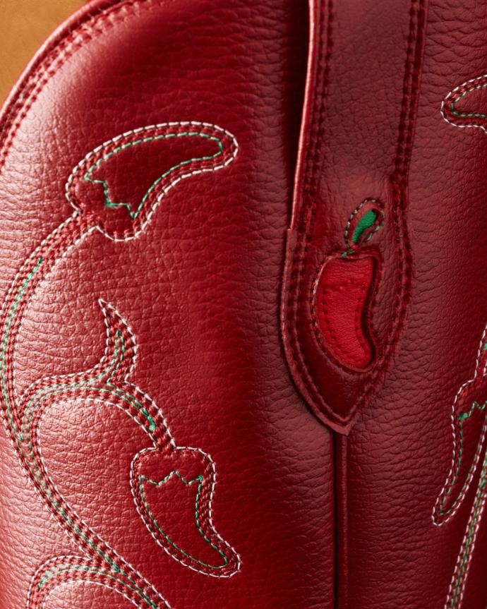 Close-up of red leather with chili pepper embroidery and stitching detail, possibly part of a cowboy boot or western-style accessory.