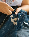 A person stitching intricate embroidery on a blue denim garment, showcasing a design that includes birds and floral elements.