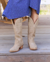 A person in a blue dress standing outdoors wearing beige cowboy boots.